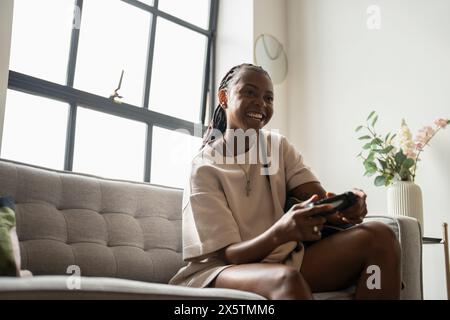 Excited young woman playing video games while sitting on sofa at home Stock Photo