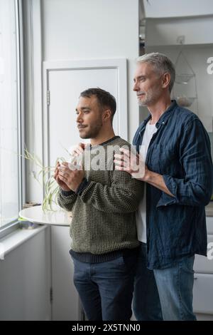 Mature male couple looking through window at home Stock Photo