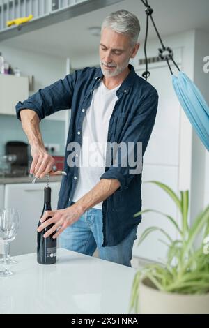 Mature man opening red wine at home Stock Photo