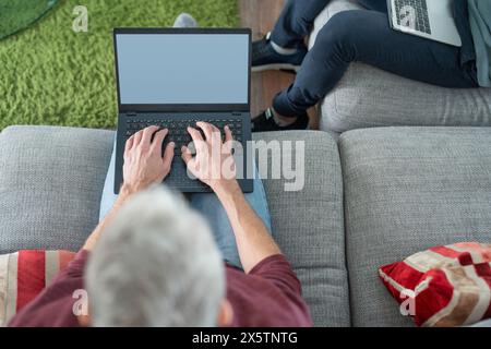 Male couple working on laptops on sofa at home Stock Photo