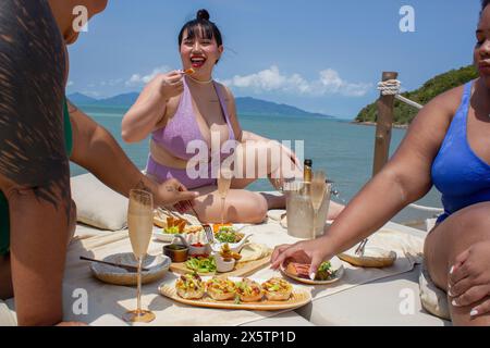 Group of cheerful women enjoying meal during picnic near bay Stock Photo