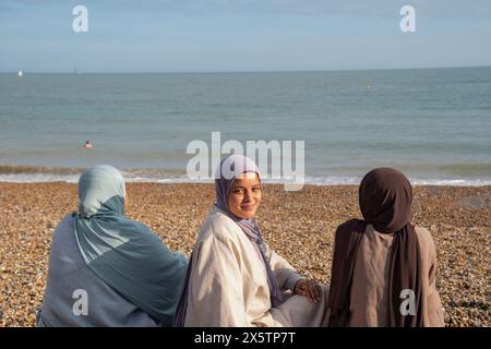 Three Muslim women sitting on beach on sunny day Stock Photo
