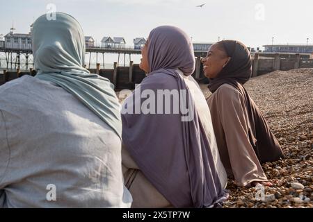 Three Muslim women sitting on beach on sunny day Stock Photo