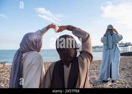 Woman photographing Muslim friends making heart shape with hands on beach Stock Photo