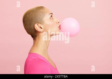 Young blond woman blowing pink balloon Stock Photo