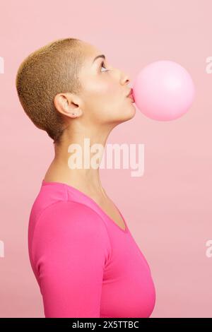 Young blond woman blowing pink balloon Stock Photo