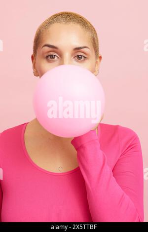 Young blond woman blowing pink balloon Stock Photo