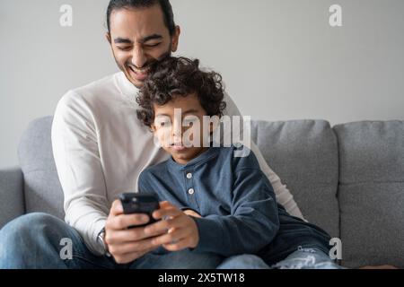 Father and son (6-7) using smart phone at home Stock Photo