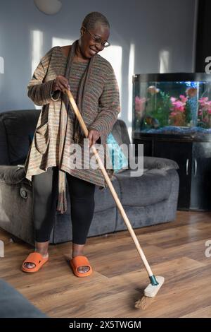 Mature woman sweeping floor in living room Stock Photo