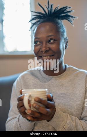 Happy woman sitting on sofa with cup of coffee Stock Photo