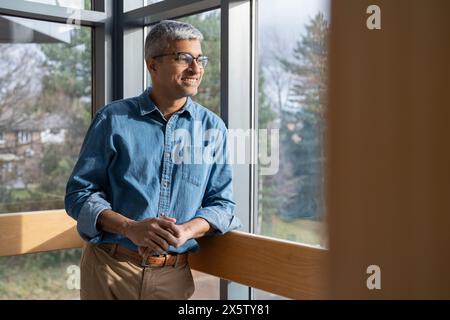 Smiling mature businessman looking through office window Stock Photo