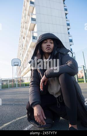 Portrait of woman in overcoat with hood crouching on basketball court Stock Photo