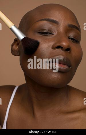 Studio portrait of woman with shaved head applying blush Stock Photo