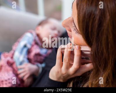 Close-up of woman holding baby son  and talking on smart phone Stock Photo