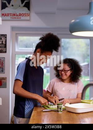 Sisters (14-15, 16-17) cutting vegetables in kitchen Stock Photo