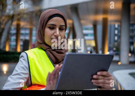 UK, London, Female engineer in hijab and hardhat using digital tablet Stock Photo