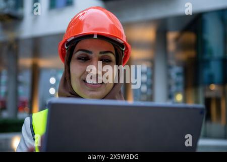 UK, London, Female engineer in hijab and hardhat using digital tablet Stock Photo