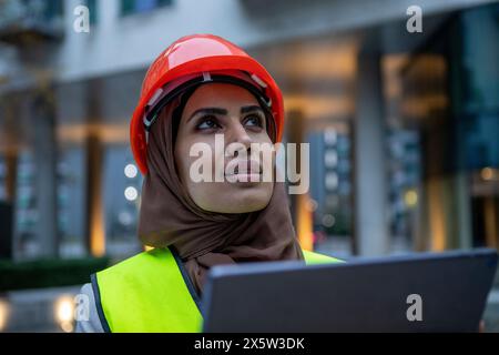 UK, London, Female engineer in hijab and hardhat using digital tablet Stock Photo
