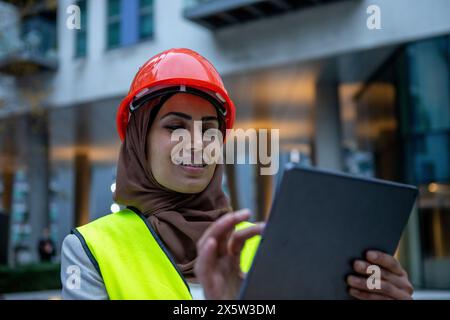 UK, London, Female engineer in hijab and hardhat using digital tablet Stock Photo