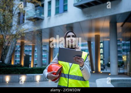 UK, London, Female engineer in hijab holding tablet on front of modern building Stock Photo