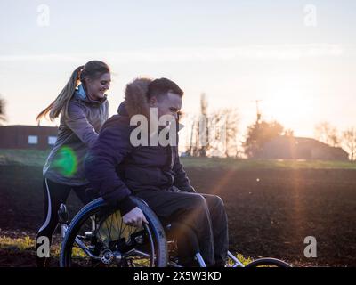 Smiling woman and man on wheelchair in field at sunset Stock Photo