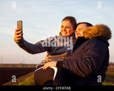 Smiling man on wheelchair with woman on laps taking selfie Stock Photo