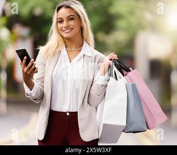 Shopping spree, woman and portrait with smartphone for fashion, retail therapy and happy outdoors. Female person, smiling and paper bags in city while Stock Photo
