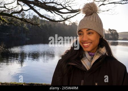 Smiling young woman in knit hat at lake Stock Photo