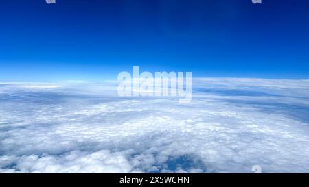 Flying high above the clouds over the Atlantic big blue ocean with big fluffy white clouds and blue skies on a clear day. Stock Photo