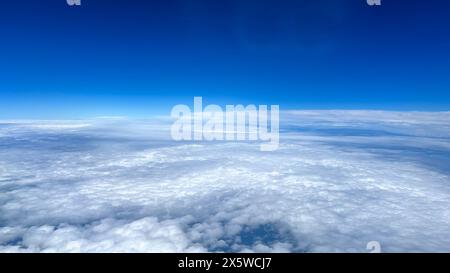 Flying high above the clouds over the Atlantic big blue ocean with big fluffy white clouds and blue skies on a clear day. Stock Photo
