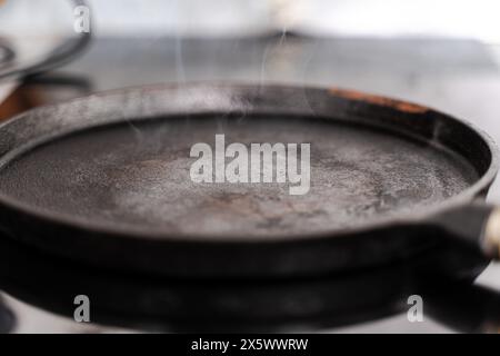 An empty pan is heated and smoking, ready to cook. Cast iron frying pan on an induction hob. selected focus. High quality photo Stock Photo