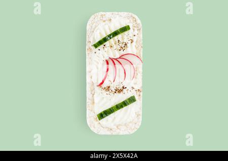 Rice cake topped with soft cheese, cucumber and radish on plain green background Stock Photo