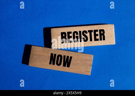 Register now words written on wooden blocks with blue background. Conceptual register now symbol. Copy space. Stock Photo