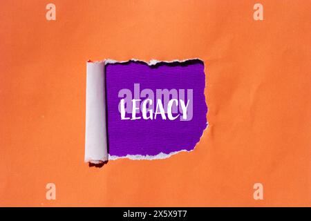 Legacy word written on ripped orange paper with purple background. Conceptual legacy symbol. Copy space. Stock Photo