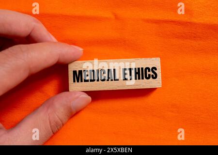 Medical ethics words written on wooden block with orange background. Conceptual medical ethics symbol. Copy space. Stock Photo