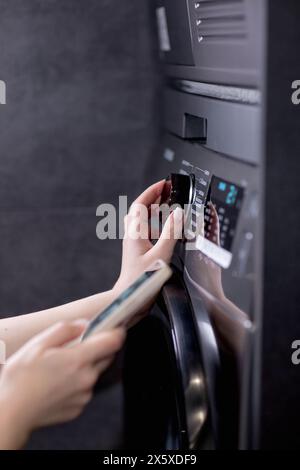 Woman controls washing machine with a phone. Stock Photo