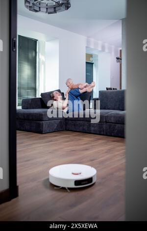 Robotic vacuum cleaner cleaning the living room while mother and son playing. Stock Photo