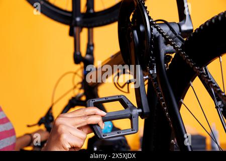 Close-up shot of african american person mending bicycle and performing annual maintenance. Detailed view of pair of hands servicing and adjusting bike pedals for leisure cycling. Stock Photo