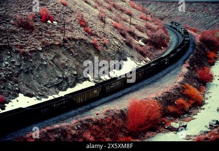 Freight train rounds a steep mountain bend alongside the Spanish Fork River, part of the famed Central Corridor in Utah. Captured on color infrared fi Stock Photo