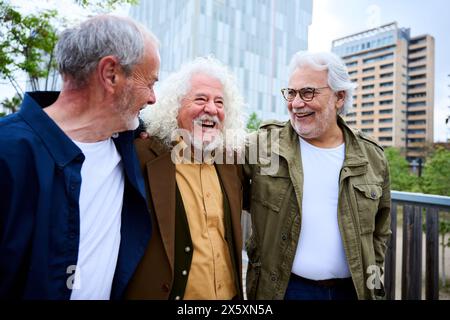 Group of three mature caucasian men enjoying embracing walk together laughing outdoor Stock Photo