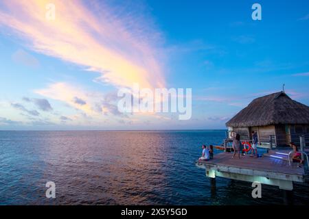 Tourists watching the sunset from a bungalow on stilts, Manava Beach Resort, Moorea, Society Islands, French Polynesia Stock Photo