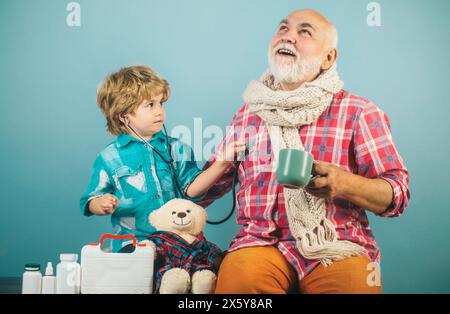 Kid helps senior man to take his pills. Man in knitted colorful scarf with medicine. Little doctor ready to examine. Stock Photo