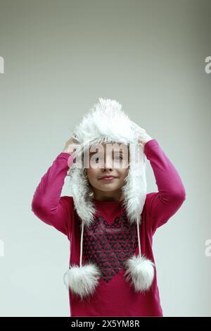 Enthusiastic young girl in a pink sweater and white fur hat shows her excitement for the holiday season with a bright smile Stock Photo