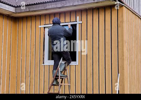 Installation of external metal slopes on window of wooden rural house, outdoor work of construction worker. Stock Photo