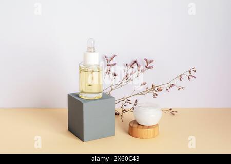 Cosmetic serum and cream in a jar and purple kermek flowers on beige table. Natural cosmetics concept. Closeup. Stock Photo