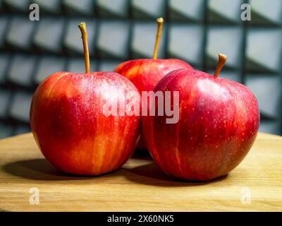 Fresh Apples on Display. Three red apples with stems on a wooden surface. Stock Photo