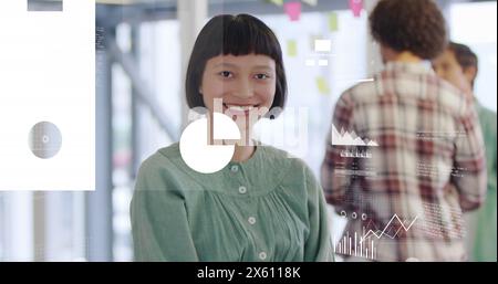 Image of graphs, map, flowchart, cloud in laptop over smiling biracial woman standing in office Stock Photo