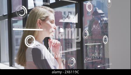 Image of graphs, changing numbers, loading circles bars, circles, thoughtful caucasian woman Stock Photo