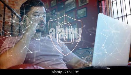 Image of padlock in shield, connected dots, biracial man talking on cellphone while using laptop Stock Photo