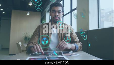 Image of icon in circles over biracial man sitting on chair and looking at camera in office Stock Photo